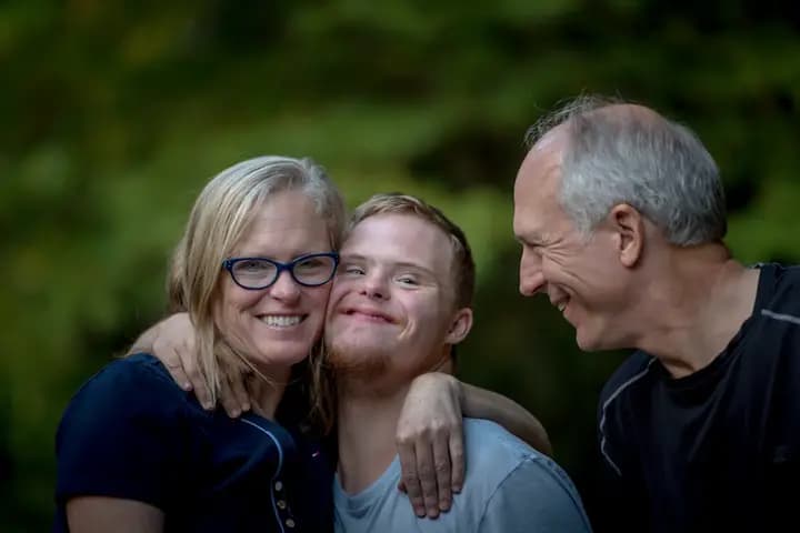 Une famille souriante entourant un jeune homme en situation de handicap